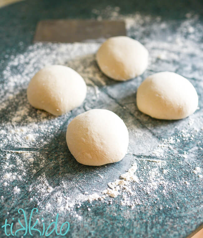 Four Neapolitan Pizza Dough balls on a lightly floured surface.