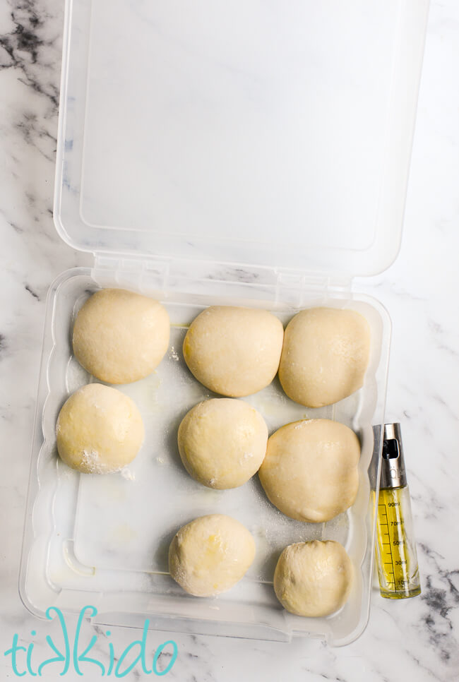 Eight neapolitan pizza dough balls in a plastic proofing box on a white marble surface.
