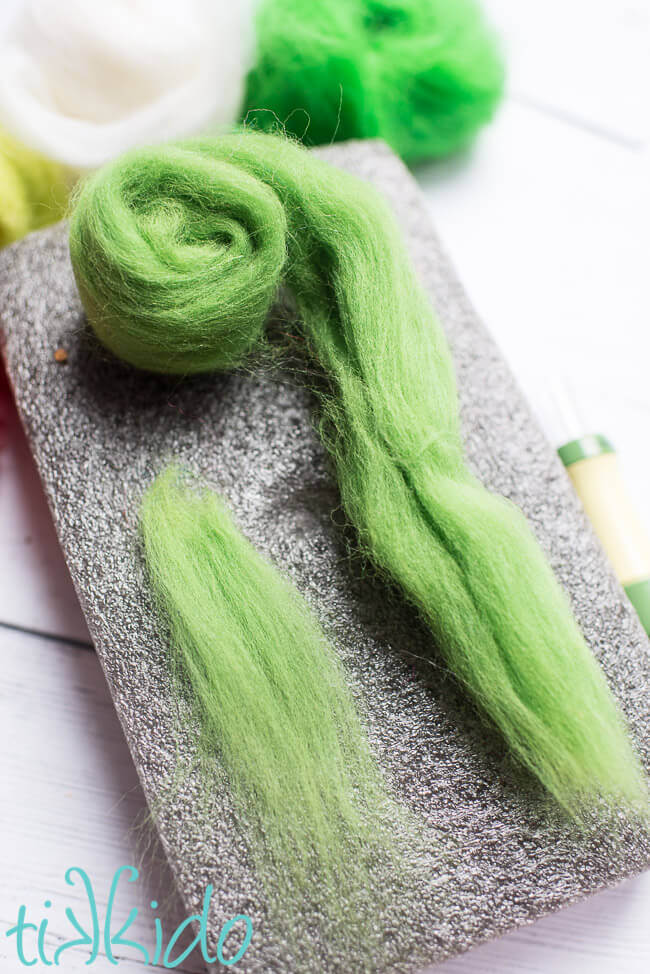 green wool roving pulled apart on a needle felting mat to make felt balls.