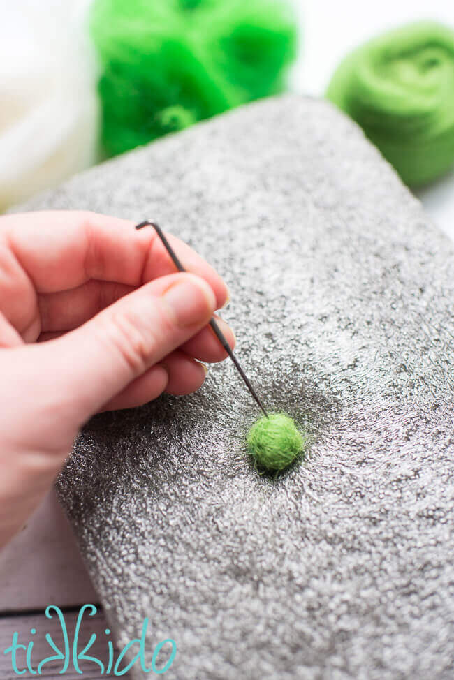 Making a green felt ball by needle felting on a needle felting mat.