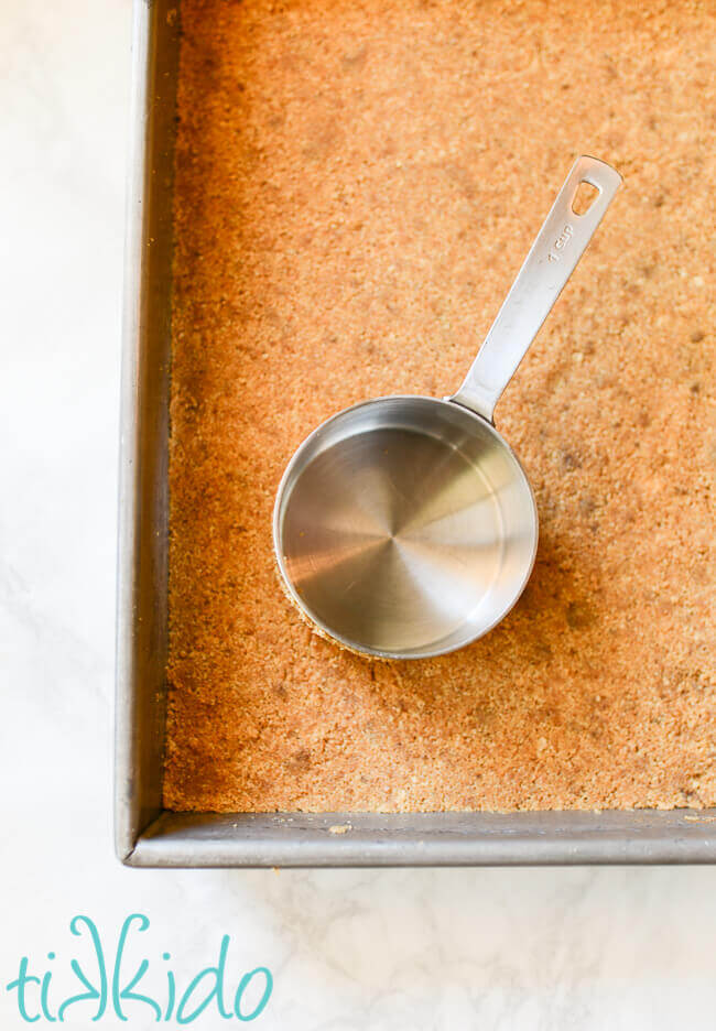 Graham cracker crust being pressed into a 9x13 pan.