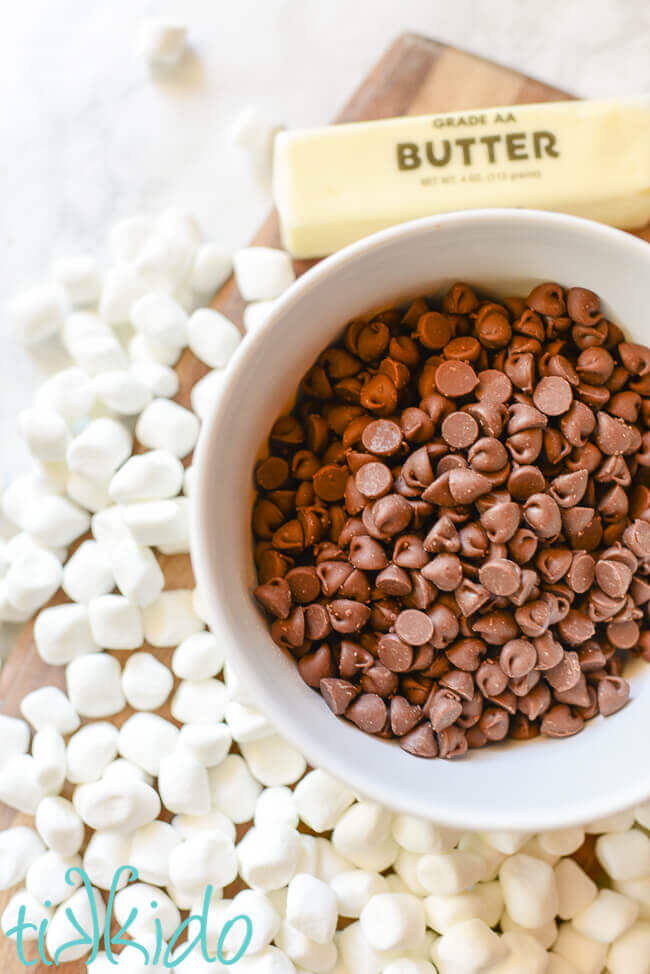 Chocolate chips, butter, and mini marshmallows on a wooden cutting board.