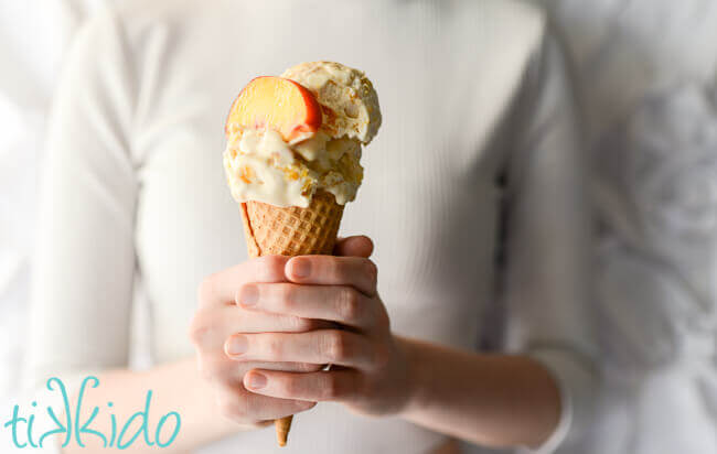 Woman holding an ice cream cone of homemade peach ice cream.