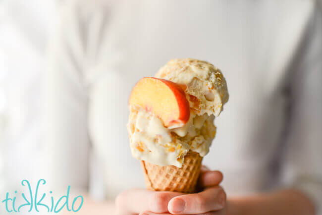 Person holding an ice cream cone with two scoops of no churn peach ice cream.