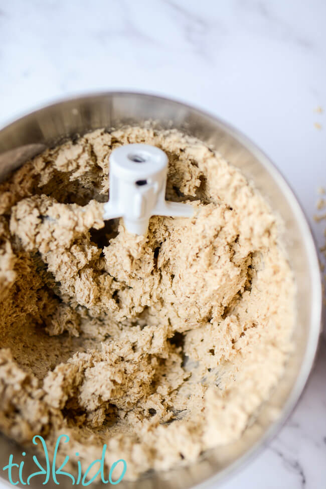 Oatmeal cookie dough for making chewy oatmeal cookies in a silver bowl with a beater.