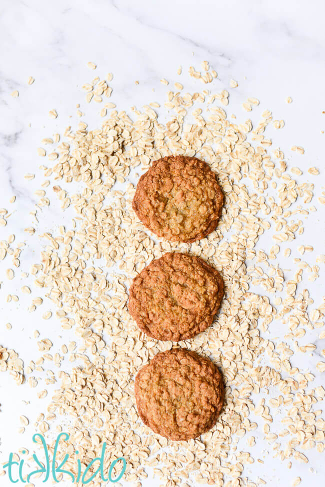 Three oatmeal cookies surrounded by uncooked oats.