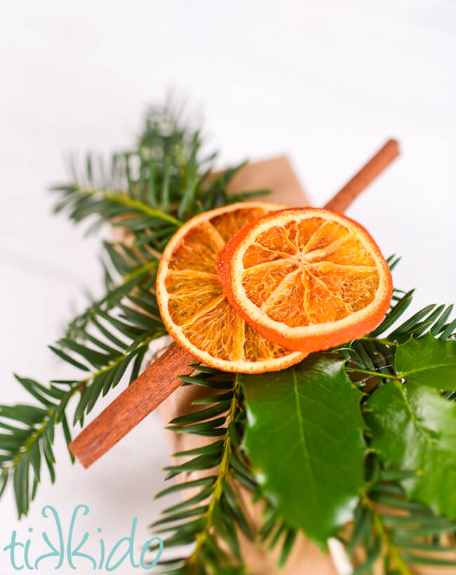 Closeup of a Dried Orange Slice Gift Topper made with fresh evergreen, holly, cinnamon sticks, and dried orange slices.