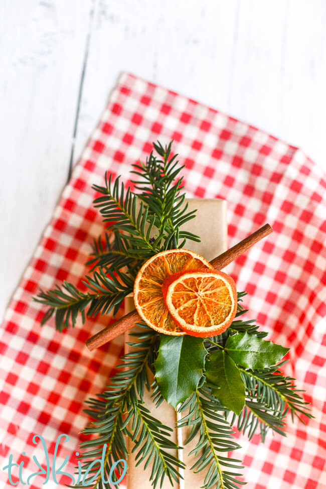 Dried Orange Slice Gift Topper on a package wrapped in brown paper, sitting on a red and white gingham piece of fabric.