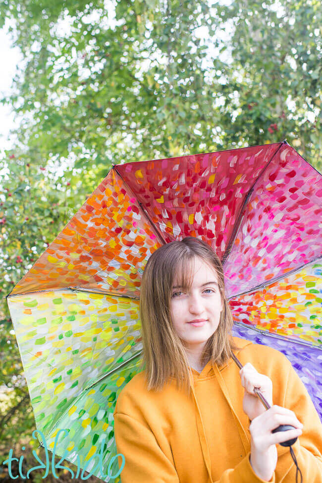 Girl holding a painted umbrella painted in an abstract rainbow pattern.