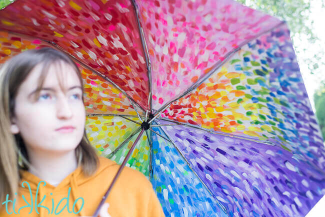 Girl holding painted umbrella painted with acrylic paints in an abstract rainbow pattern.