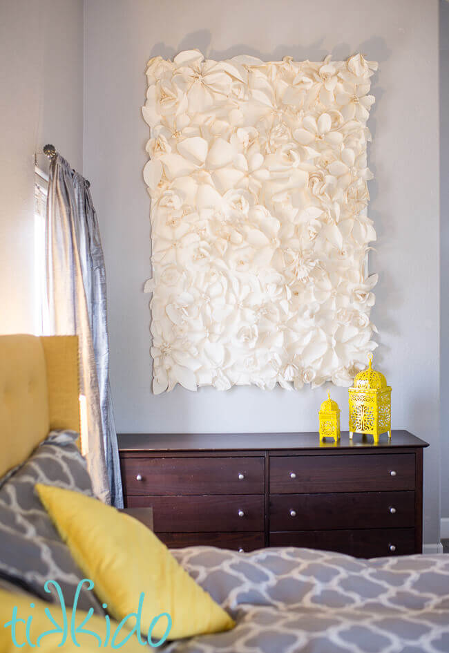 Paper flower wall decoration hanging on a grey bedroom wall over a dark wood dresser.