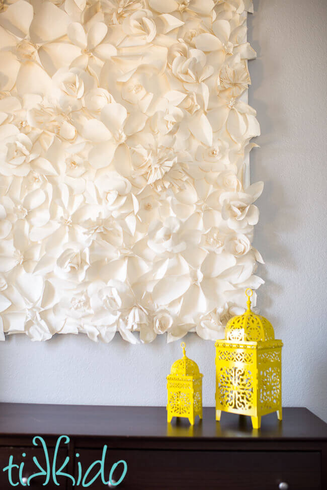 Paper flower wall decoration made with white paper, hanging on a light grey wall.