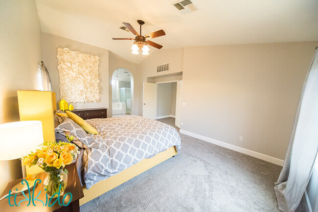 Large scale paper flower wall decoration hanging in a yellow and grey master bedroom.