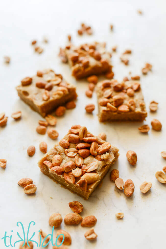 Peanut butter bar cookies on a white marble background surrounded by peanuts.