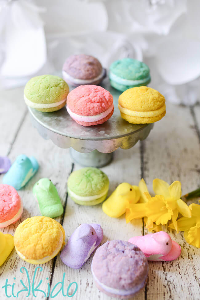 Five Peeps Whoopie pie sandwich cookies on a galvanized metal cake stand, surrounded by five Peeps candies in five different colors.