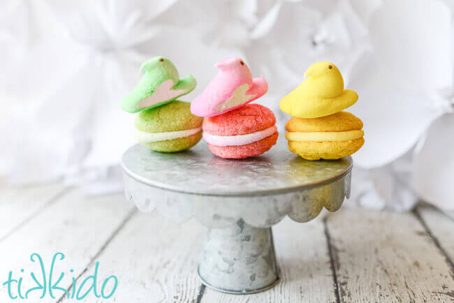 three Peeps Whoopie pie sandwich cookies on a galvanized metal cake stand, with matching colored peeps balancing on top of each cookie.
