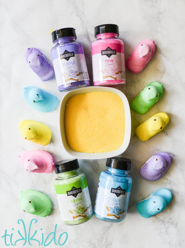 A rainbow of peeps surrounding bottles and a bowl of colored sugar that match the peep colors.