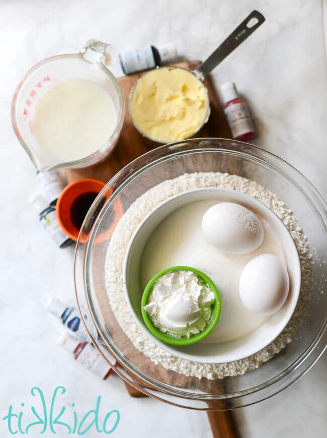 Ingredients for soft sugar cookies, displayed on a wooden cutting board on a white marble background.