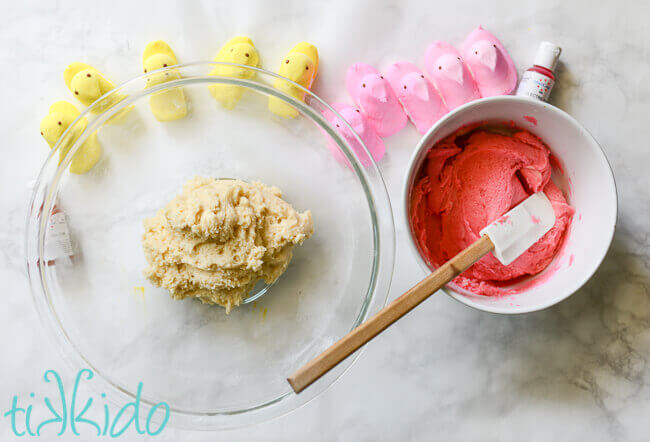 Yellow and pink Peeps surrounding two bowls, one clear glass with uncolored sugar cookie dough, one white with pink sugar cookie dough and a spatula.