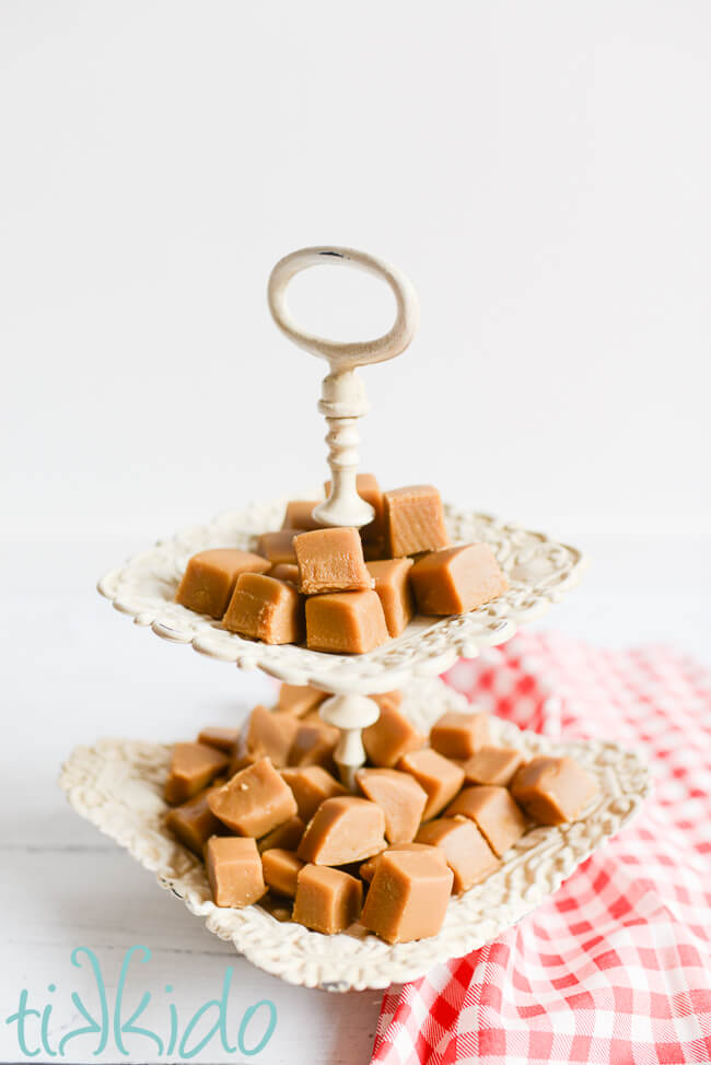 Two tiered white tray filled with penuche fudge, next to a red and white checked cloth.