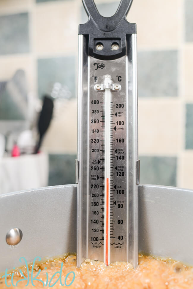 Pralines cooking in a saucepan with a candy thermometer coming close to the soft ball stage.