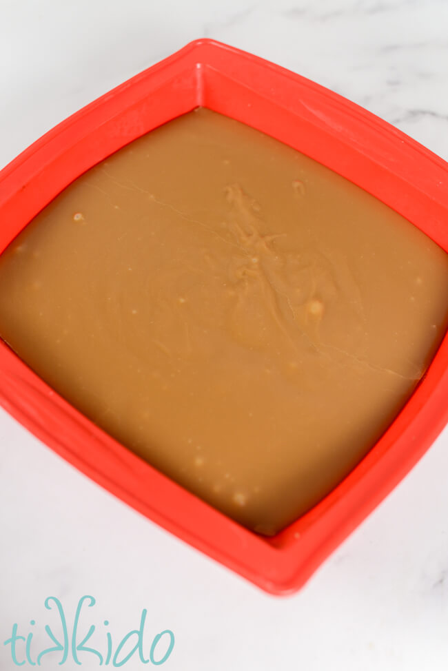 Penuche fudge setting in a red silicone pan sitting on a white marble counter.