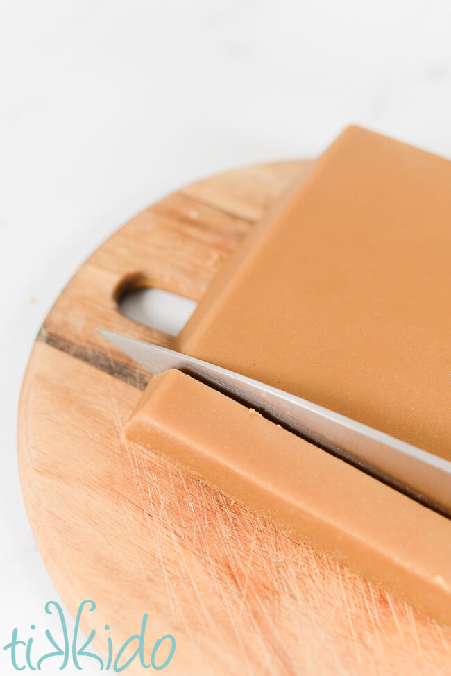 Penuche Fudge being cut into pieces with a large knife on a wooden cutting board.