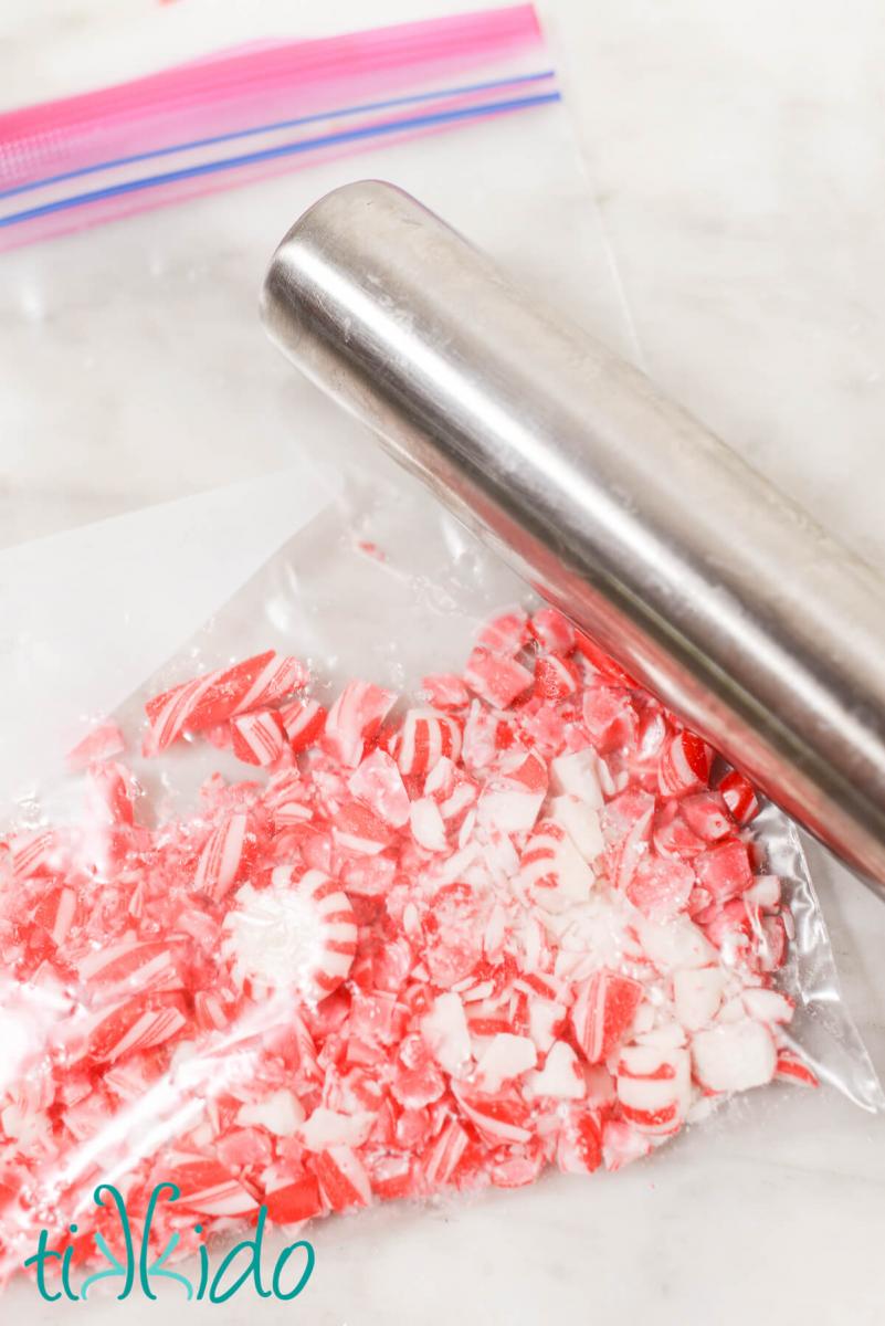 Peppermint candies in a ziplock bag being crushed with a silver rolling pin.