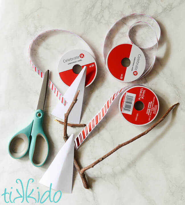 Ribbon, cardstock, sticks, and scissors on a white marble background.