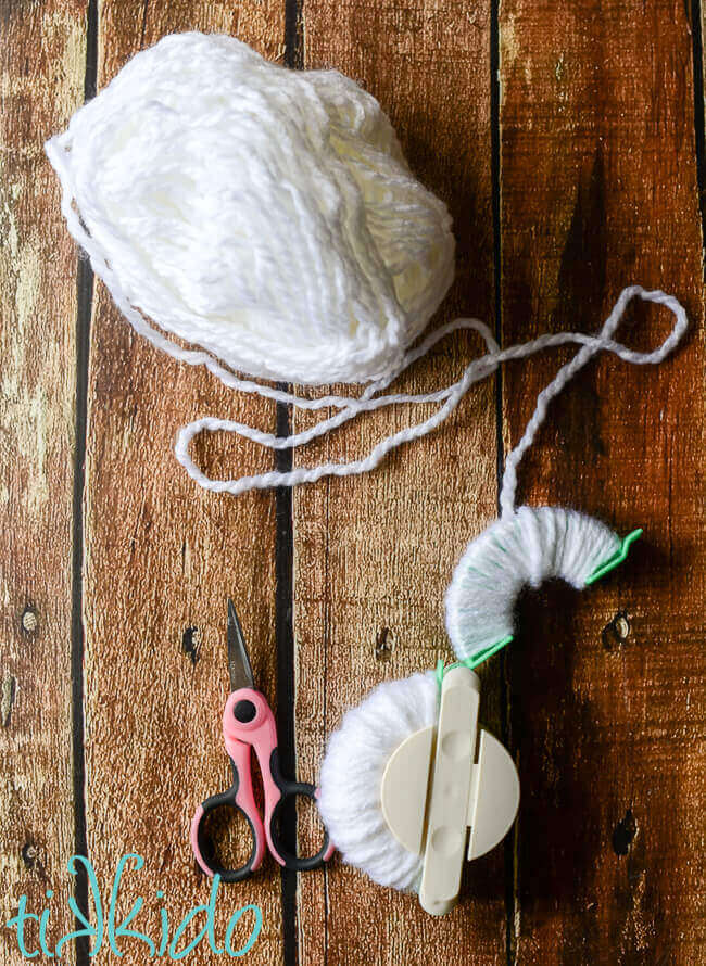 White yarn being wound around a pom pom maker tool to make snowball pom poms for a DIY Snowball Fight toy