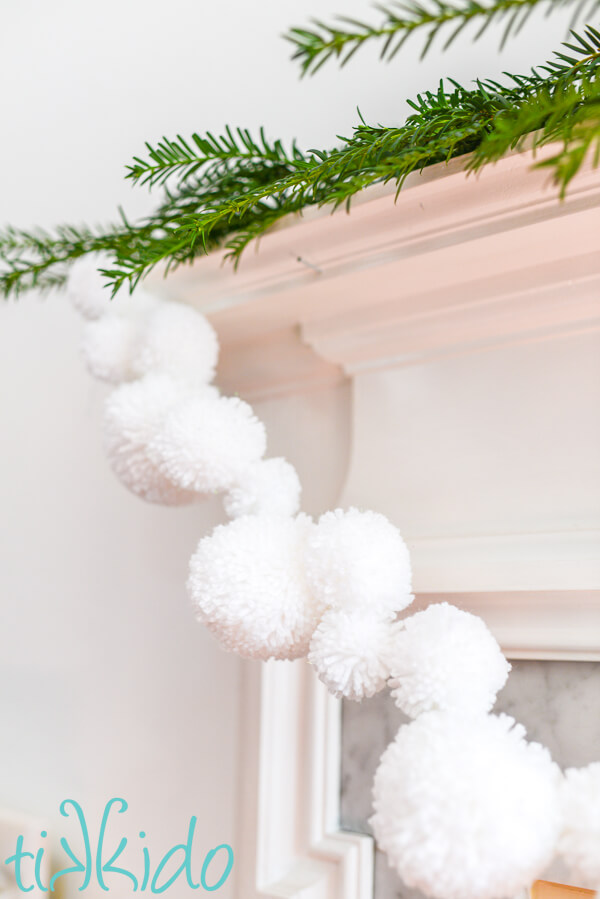 White pom pom garland hanging from a white fireplace mantel.
