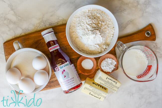 Ingredients for prickly pear cupcakes displayed on wooden cutting board on white marble backdrop.