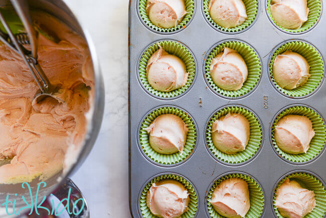Pink prickly pear cupcake batter scooped in cupcake liners in cupcake tin.  Bowl of batter and scoop beside tin.