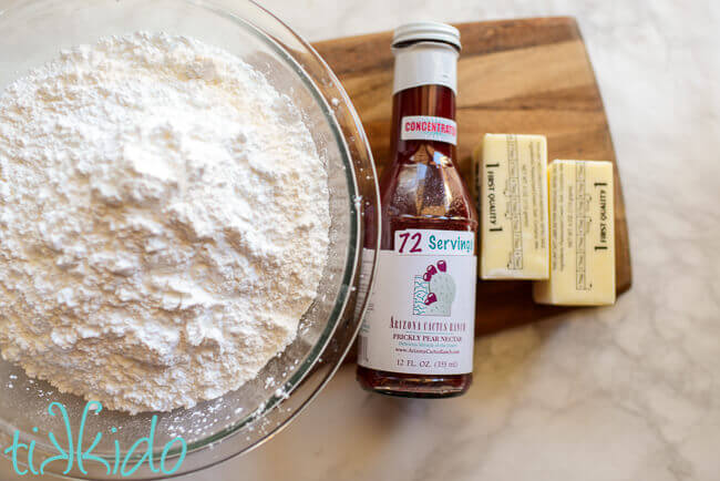 Powdered sugar, prickly pear juice, and butter on a wooden cutting board.