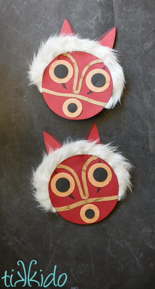 Two paper princess Mononoke masks on a black chalkboard background.