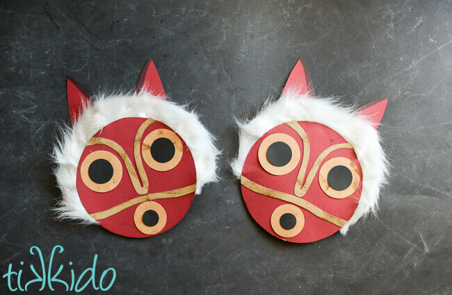 Two paper princess Mononoke masks on a black chalkboard background.