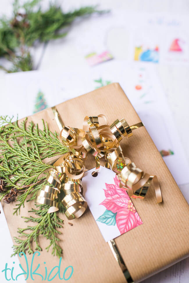 Printable Christmas Gift Tag on a christmas present wrapped with brown kraft paper, gold ribbon, and fresh evergreen.