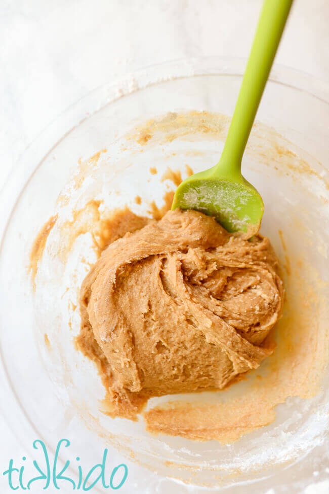 Clear bowl containing pumpkin biscotti cookie batter, being mixed with a green spatula.