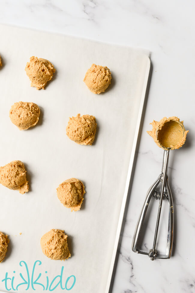 Pumpkin cookie dough scooped on a parchment lined cookie sheet.