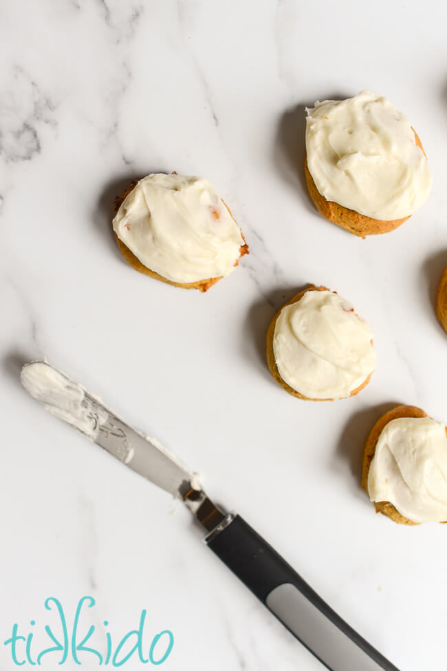 Soft pumpkin cookies being frosted with cream cheese icing.