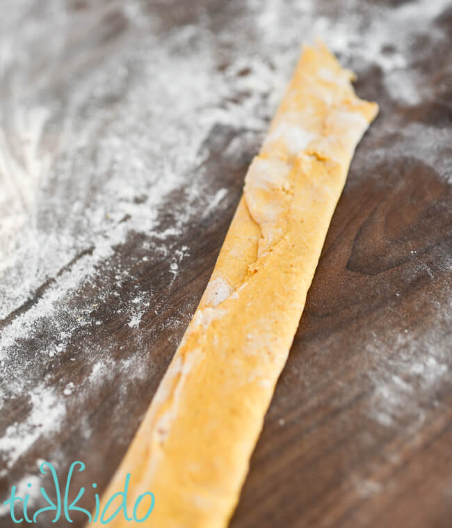 Pumpkin pasta dough folded on itself on a floured countertop.