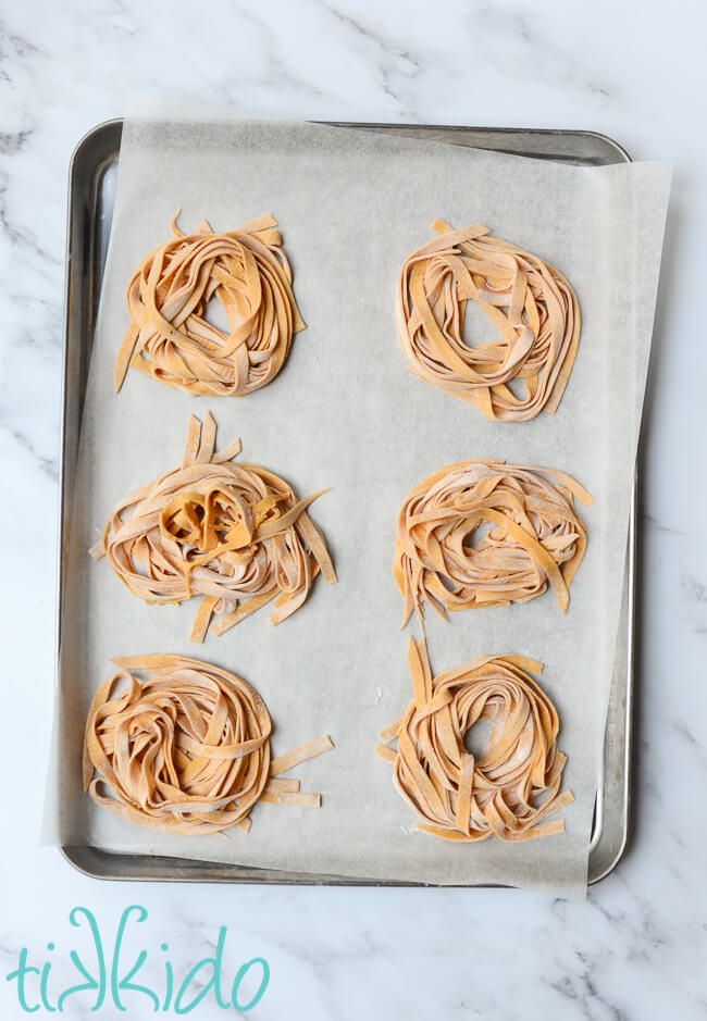 Homemade pasta made with pumpkin pasta dough on a parchment lined baking sheet.