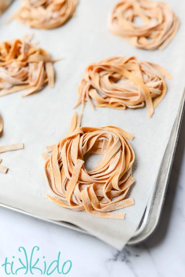 Homemade pumpkin pasta noodles on a parchment lined baking sheet.
