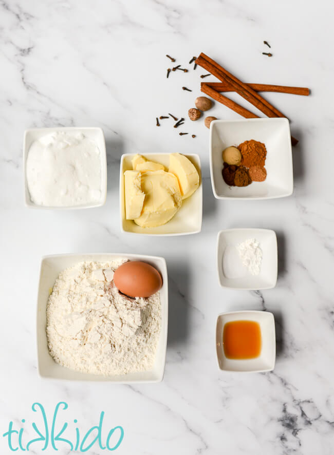 Ingredients for Pumpkin Spice Sugar Cookie recipe in bowls on a white marble surface.