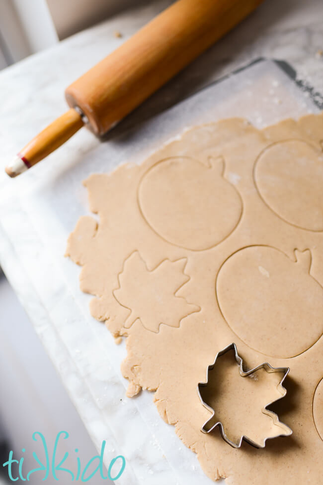 Pumpkin Spice Sugar Cookie dough being cut into shapes with fall cookie cutters.