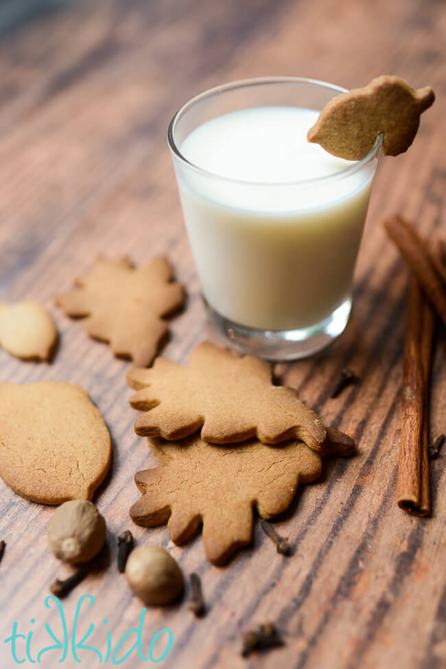 Pumpkin Spice Sugar Cookies and whole pumpkin pie spices on a table next to a glass of milk with a pumpkin spice cookie shaped like an acorn balancing on the rim.