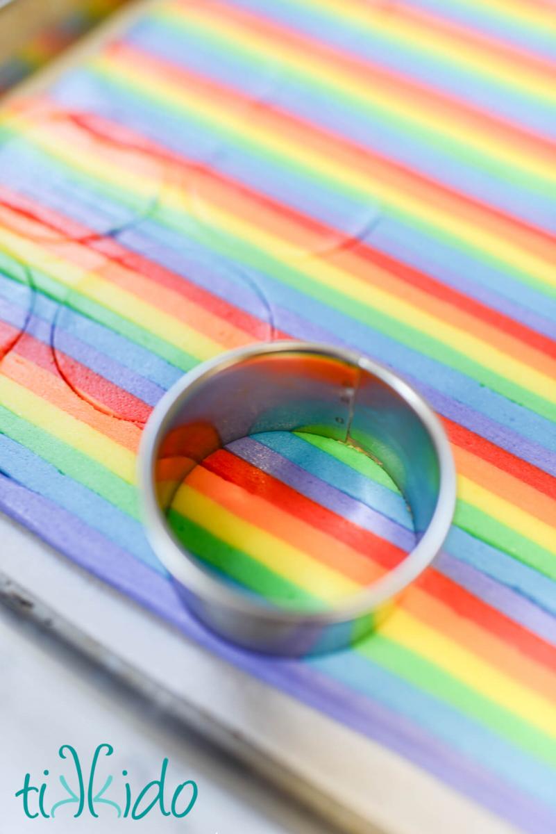 Rainbow frosting being cut into circles with a round cookie cutter to make the icing filling for homemade rainbow oreos.