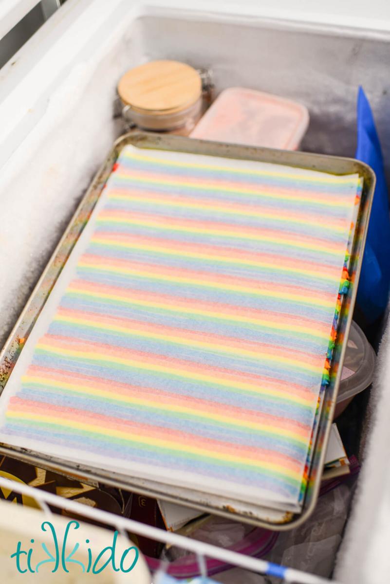 American buttercream icing piped in rows of rainbow colors on a parchment lined sheet pan, sitting in a chest freezer.