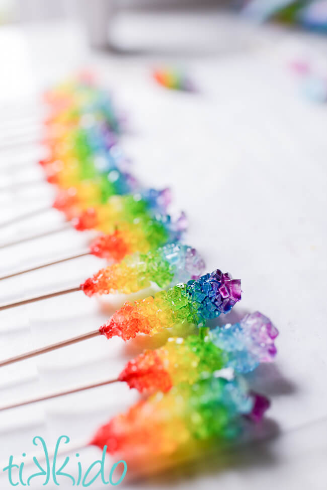 Rainbow rock candy painted with food coloring, drying on parchment paper.