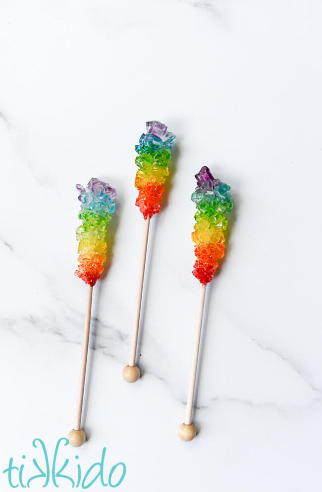 Three sticks of rainbow rock candy on white marble.